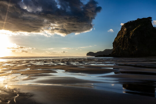 Lion Rock reflected on the black sand at Piha Beach, Auckland, New Zealand