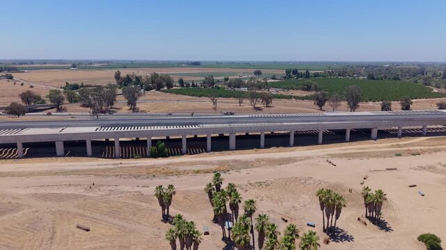 Descending Aerial Drone Shot Over California High Speed Rail Construction With Freeway Traffic Palm Trees Overpass and Farmland