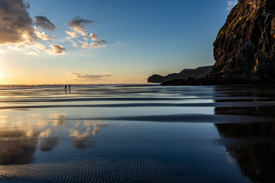 Couple walking at sunset on Piha Beach, Auckland, New Zealand