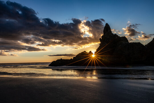 Sunstar through Lion Rock at sunset on Piha Beach, Auckland, New Zealand