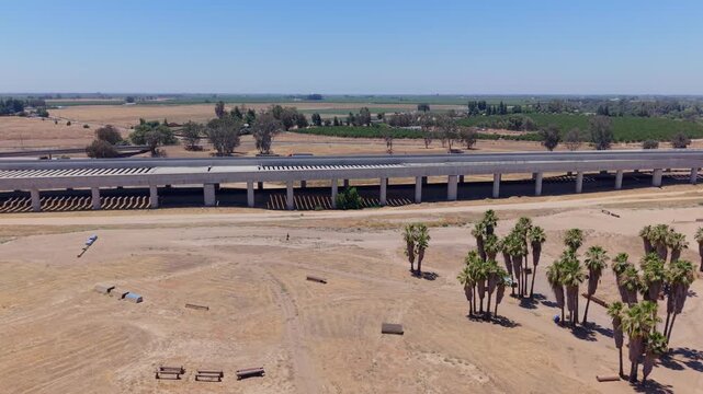 Descending and Panning Aerial Drone Shot Right to Left Over California High Speed Rail Construction With Freeway Traffic Palm Trees Overpass and Farmland
