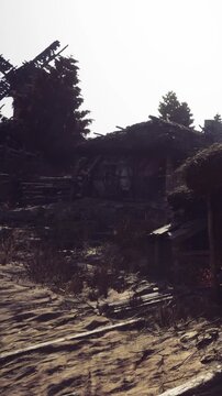 An empty dirt path leads to old buildings surrounded by trees and debris. The sun sets, casting long shadows over the ground. The area shows signs of decay and neglect.