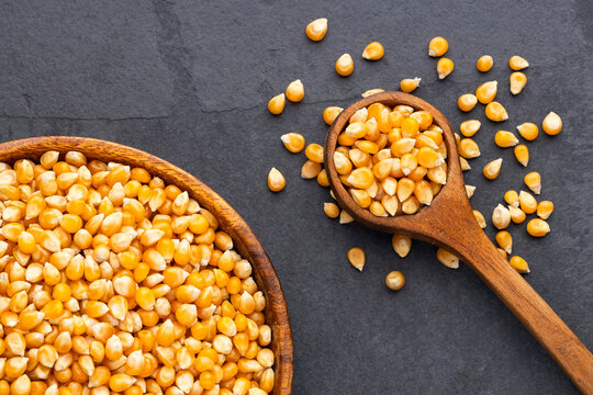 Popcorn kernels in a wooden spoon and bowl on a black chalkboard background with space for text