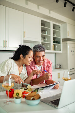 Smiling couple taking online cooking class in home kitchen