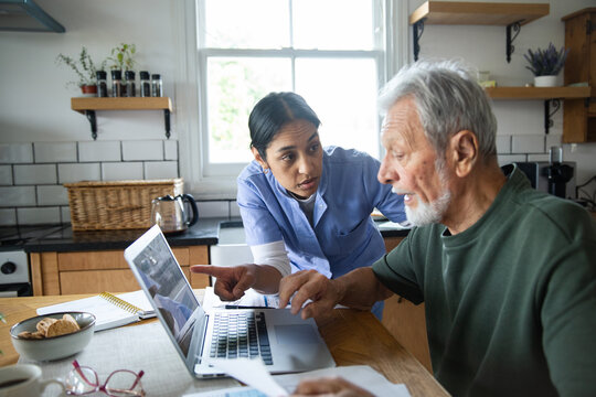 Caregiver helping senior man with laptop in home kitchen