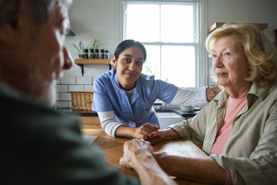 Home caregiver comforting elderly couple in kitchen
