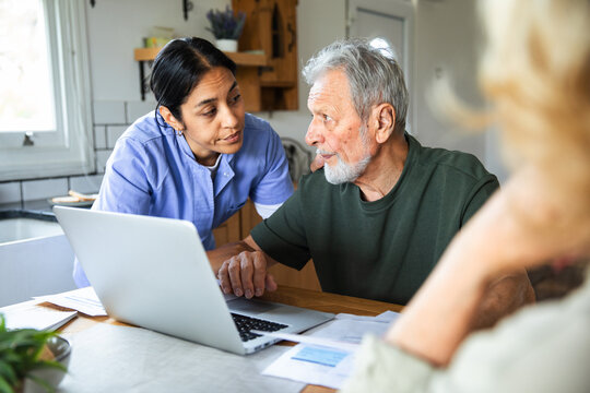 Caregiver helping senior man with laptop at home