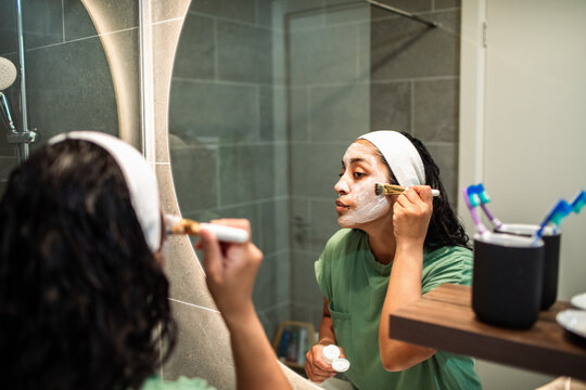 Woman applying facial mask in home bathroom mirror