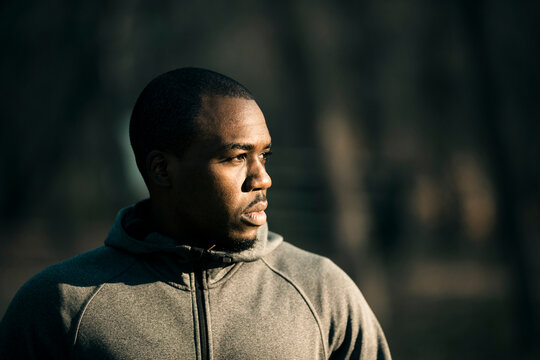 Pensive man in gray hoodie looking away outdoors in park