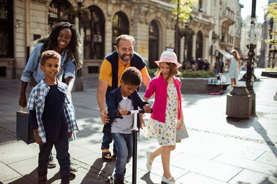 Happy family with children riding scooter on city street