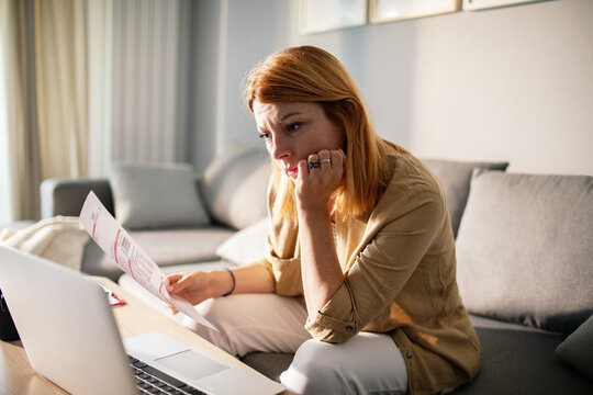 Concerned woman reviewing bills at home with laptop