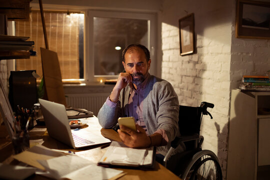 Man in wheelchair using smartphone at home office at night