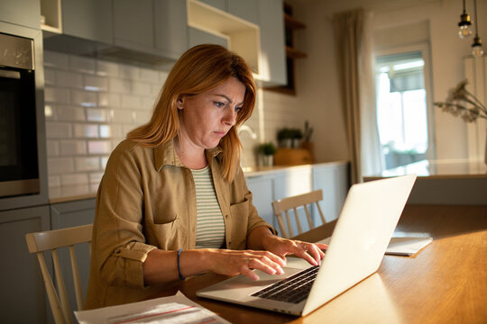 Focused woman working on laptop at home kitchen table