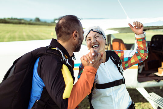 Senior woman and instructor celebrating after skydiving at rural airfield