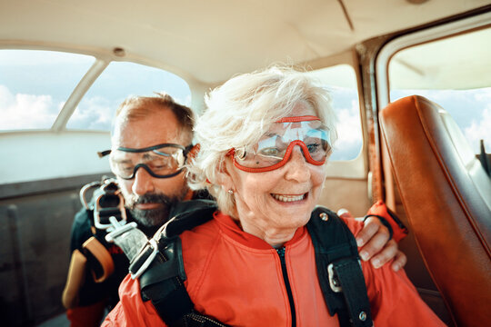 Smiling senior woman with instructor ready for tandem skydive in airplane