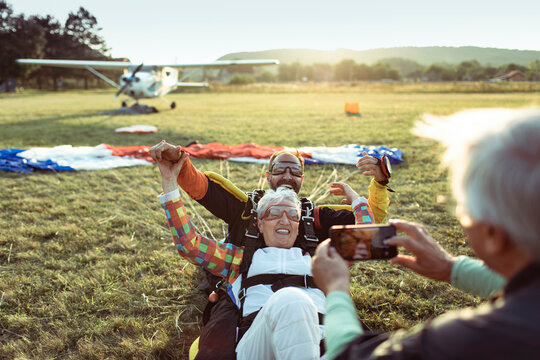 Senior couple celebrates tandem skydiving landing at rural airfield