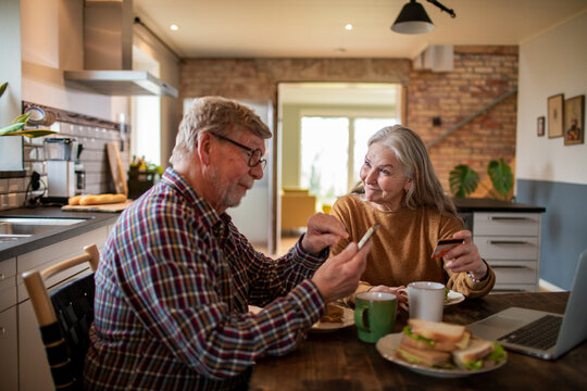 Senior couple making online payment in home kitchen