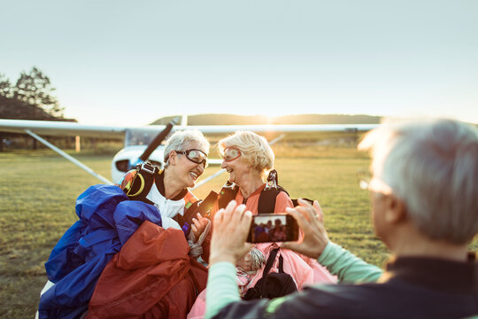 Two senior women celebrating after skydiving on airfield at sunset