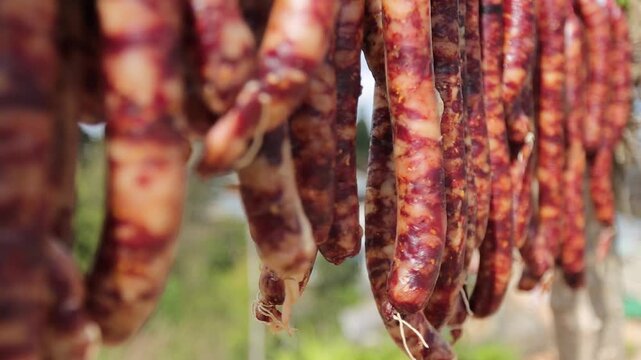 Close-up of traditional Chinese cured pork sausages hanging outdoors to air dry under natural sunlight. Known as Chinese lap cheong, Yunnan sausage, or Sichuan-style cured sausage, this preserved meat