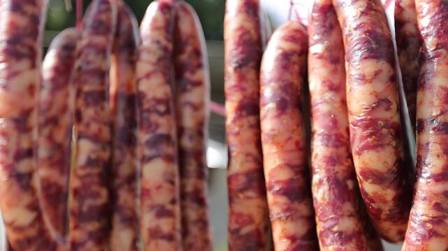 Close-up of traditional Chinese cured pork sausages hanging outdoors to air dry under natural sunlight. Known as Chinese lap cheong, Yunnan sausage, or Sichuan-style cured sausage, this preserved meat