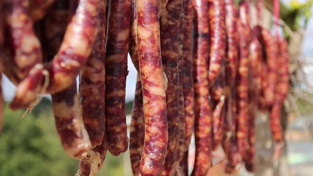 Close-up of traditional Chinese cured pork sausages hanging outdoors to air dry under natural sunlight. Known as Chinese lap cheong, Yunnan sausage, or Sichuan-style cured sausage, this preserved meat