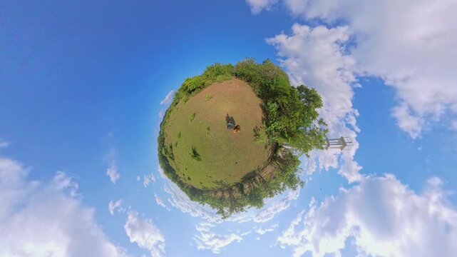 Little Planet View of Two Tourists Walking Across Open Grassy Hill Near Observation Tower, Surrounded by Blue Sky and Tropical Vegetation, Travel and Freedom