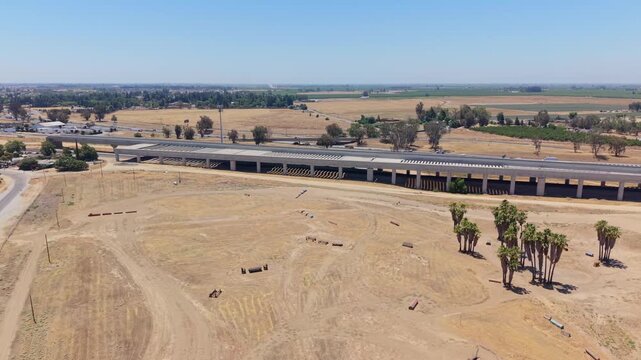 Reversing and Panning Aerial Drone Shot Left to Right Over California High Speed Rail Construction With Overpass Freeway Traffic Cell Tower and Farmland