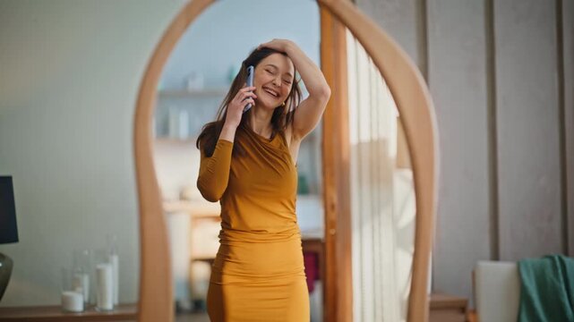 Smiling woman checking reflection wearing trendy dress talking cellphone. 