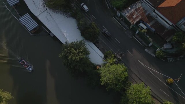 A tour boat and light traffic passing by in central Surabaya, top down aerial spinning view of river and street