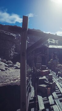 An old wooden structure located near a canyon. Wooden beams support the area. Various items are placed on the ground and around the structure. Sunlight shines on the scene.
