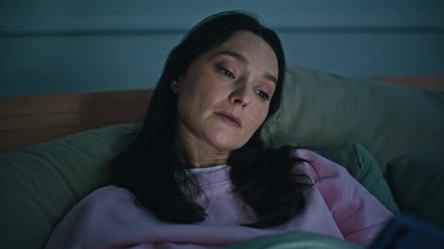 Bored lady checking phone lying bed late evening alone closeup. Sad woman
