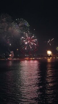 Vertical video. Colorful New Year Fireworks Illuminating a Tropical Island Coast Above Calm Sea Water at Night, Festive Holiday Celebration, Bright Reflections and Winter Vacation