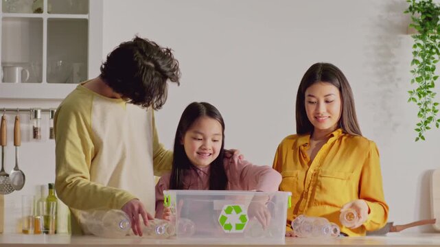 Smiling Diverse Family Including Dad, Mom, And Young Daughter Recycling Plastic Bottles Together At Home In Kitchen. Engaging In Eco-friendly Activity, Promoting Sustainability And Environmental Care.