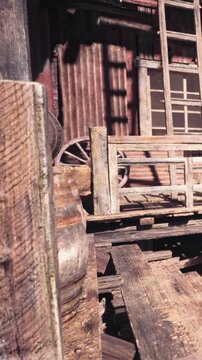 Wooden planks and barrels are stacked in a rundown building. Light shines through the gaps in the walls. The atmosphere shows signs of aging and neglect in an abandoned setting.