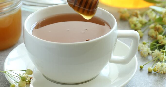 Adding natural linden honey into cup of tea at grey table, closeup