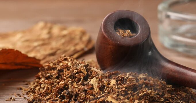 Dry tobacco, leaf, ashtray and smoking pipe on wooden table, closeup
