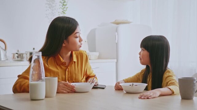 Happy Asian Mother And Daughter Engaged In Conversation While Eating Healthy Breakfast Together At Home, Sitting At Kitchen Table, Building Bonding Moments. Family Lifestyle Concept.