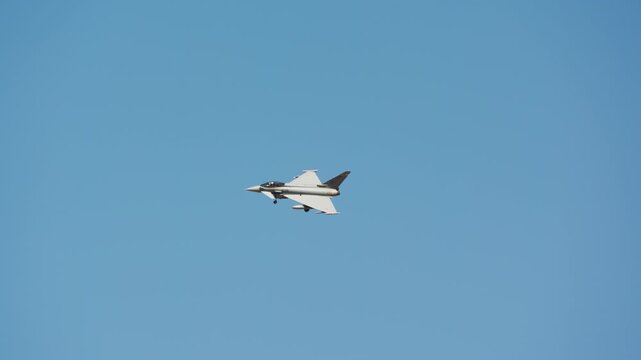 Combat aircraft in distant flight against clear blue sky, delta wing fighter with canards centered in the frame, landing gear lowered for approach, slow motion