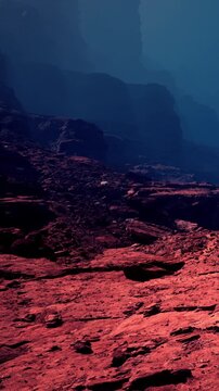 The scene shows a rocky surface with red colors. Mountains are visible in the background, and the sky appears blue. The area looks dry and barren with unique rock formations.