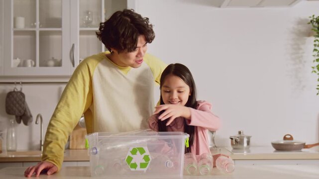 Happy Smiling Asian Girl And Young Man Enjoying Quality Time Together While Recycling Plastic Bottles In A Bright Modern Kitchen. Engaging In Eco-friendly Activities As A Family Concept.