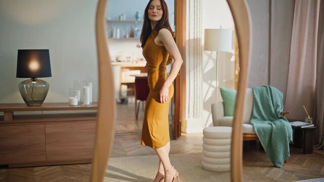 Lady trying chic dress looking mirror home. Elegant brunette checking outfit 