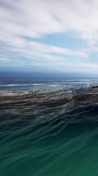 Waves roll across the water, creating foam as they reach the shore. The sky is clear with some clouds, and the scene shows a typical day at the beach.