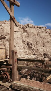 A wooden structure stands next to a rocky cliff under a bright blue sky. The sunlight illuminates the rugged landscape around the area.