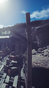 The scene shows a mining site with a wooden structure and tools. Sunlight shines over the area, highlighting the rocky surroundings. The ground has equipment for mining activities.