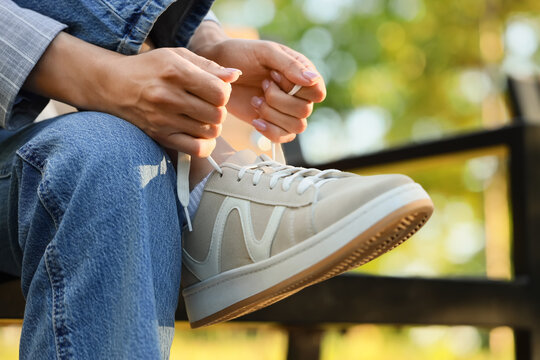 Person tying shoelaces on beige sneakers outdoors