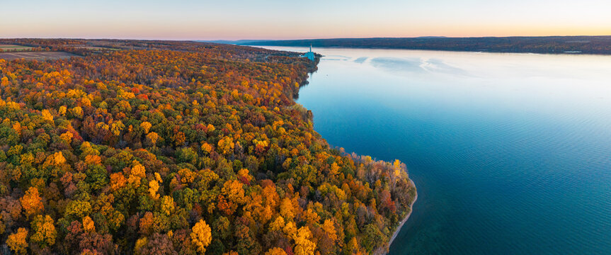 Aerial view of the vibrant autumn foliage along the shoreline of Cayuga Lake during golden hour in Ithaca, New York, United States.