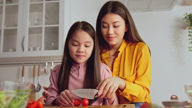Smiling Happy Asian Woman And Girl Cooking Together In Kitchen, Preparing Meal With Fresh Ingredients, Enjoying Fun Time And Building Family Bonding Over Healthy Cooking Activities.