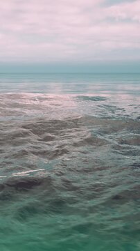Waves move gently on the surface of the ocean during sunset. The sky has clouds that reflect the colors of the fading light. The scene is tranquil and spacious, inviting calm thoughts.