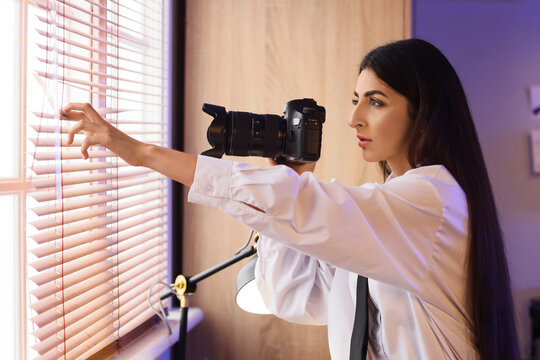 Woman photographer looking through window blinds with camera