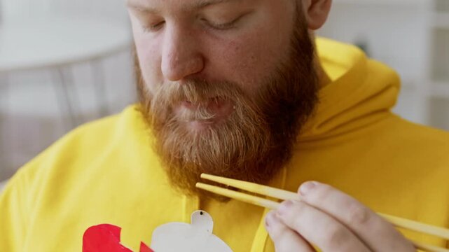 Focused Caucasian Male Enjoying Meal With Chopsticks, Sitting At Modern Kitchen Table, Embracing Healthy Eating Lifestyle. Concept Of Nutrition And Wellbeing In Vibrant Setting.